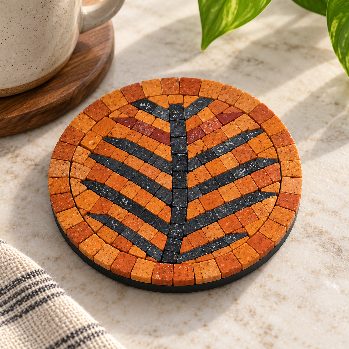 Round stone mosaic coaster with orange tiles, black tree-branch pattern, dark rim
